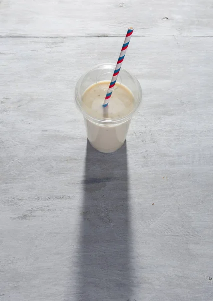 Muz milkshake Beyaz ahşap zemin üzerinde plastik kap içinde — Stok fotoğraf