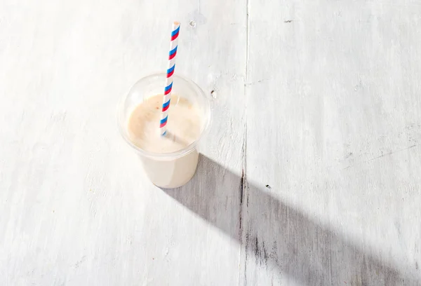 Banana milkshake em copo de plástico sobre fundo de madeira branca — Fotografia de Stock
