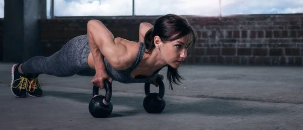 Young woman athlete in sportswear push ups with dumbbells — Stock Photo, Image