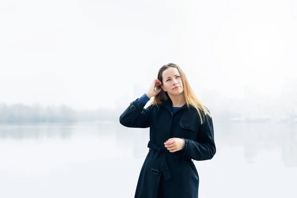 Женщина в черном пальто на городской набережной в пасмурный день — стоковое фото