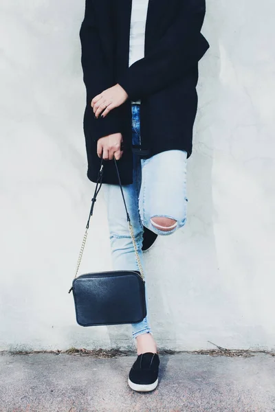 Mulher de casaco preto, jeans azul e bolsa perto da parede — Fotografia de Stock