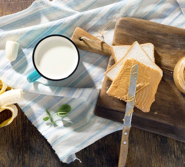 Fıstık ezmesi, muz ve ahşap masa üzerinde süt ile sandviç