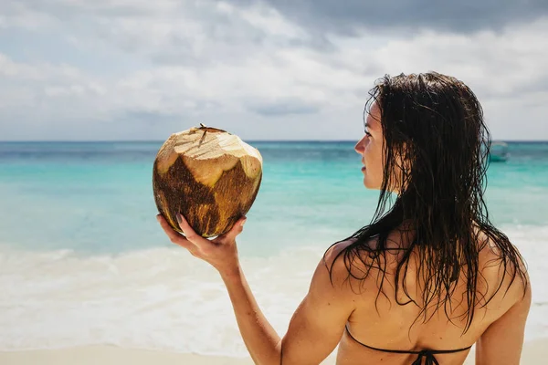 Красивая женщина на берегу океана держит свежий кокос — стоковое фото