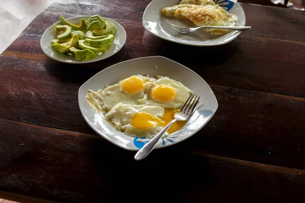 Mesa de desayuno con plato de huevos fritos, huevos revueltos y aguacate — Foto de Stock
