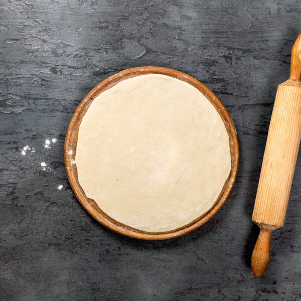 Pizza dough on round wooden board 