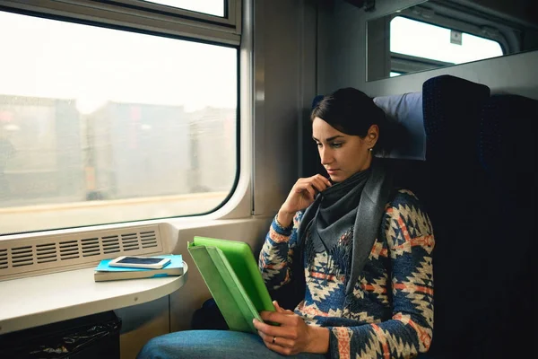 Pretty woman traveling by train sitting near the window with tablet. Enjoying travel