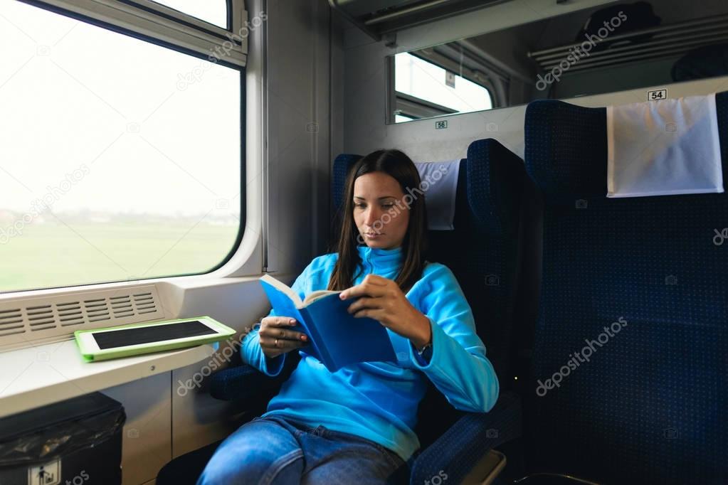 Pretty woman traveling by train sitting near the window reading a book. Enjoying travel