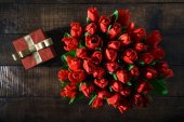 Pohled shora kytice červené tulipány s červené krabičky na tmavý dřevěný stůl s kopií prostor