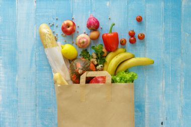 Paper bag full of different healthy food on blue background. Top view. Flat lay