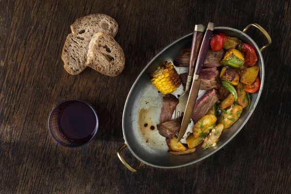 牛排配炒土豆和蔬菜 在煎锅里放上深色背景的红酒 顶部看 餐桌概念 — 图库照片