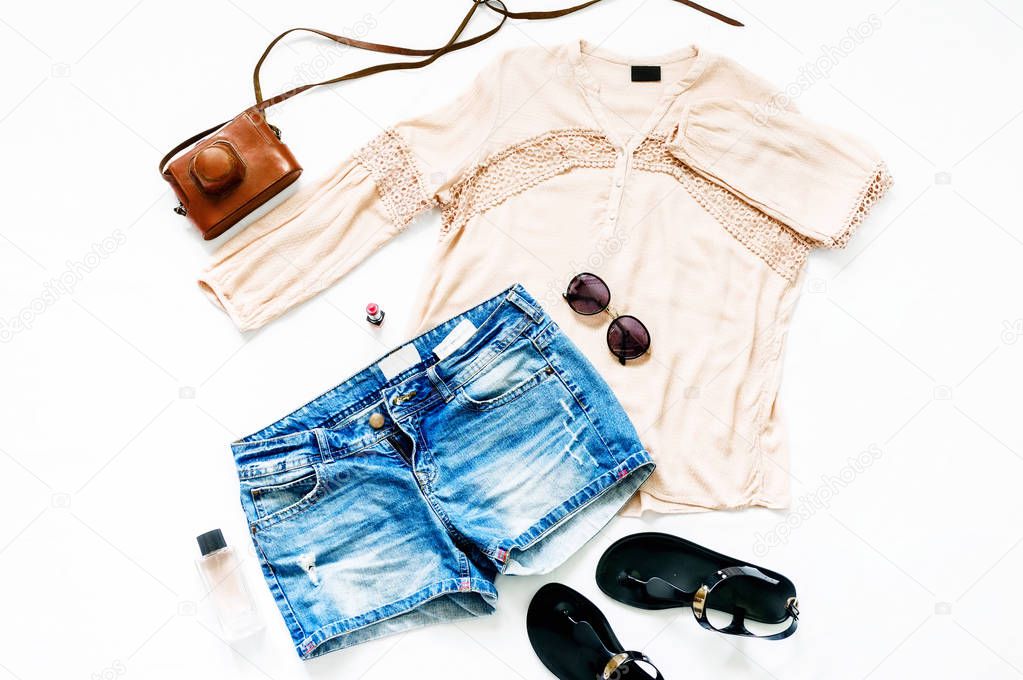 Summer set of female clothes on white background. Female denim shorts with blouse and sandals, top view, flat lay