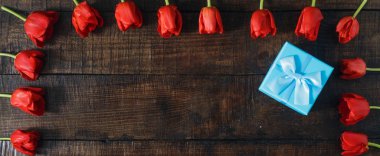 Koyu ahşap arka plan üzerinde kırmızı lale ile mavi hediye kutusu