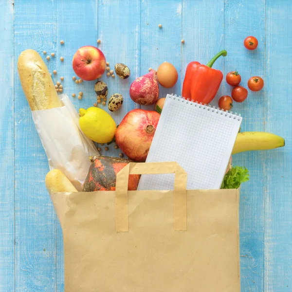 Бумажный пакет различных свежих здоровых продуктов питания ноутбук на деревянной backgro — стоковое фото