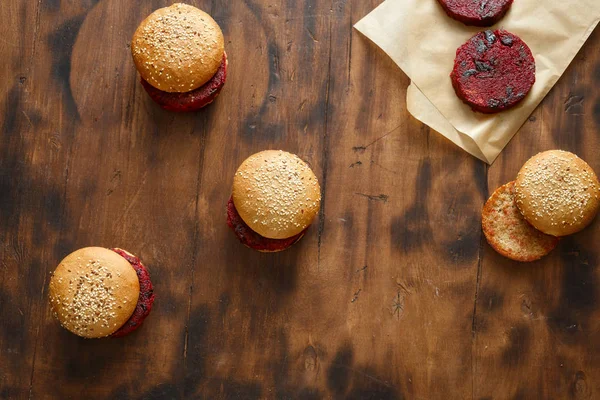Vegetarian burgers with beet cutlets with prunes on dark wooden table, top view