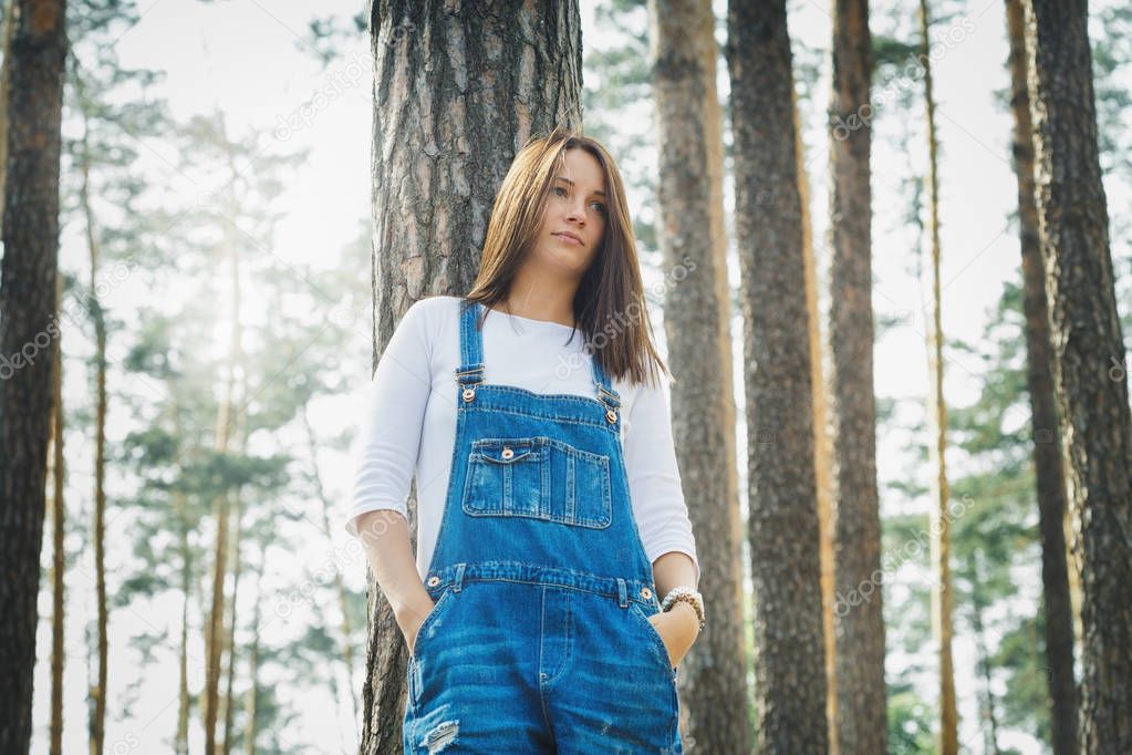 Beautiful young girl in denim overalls in the forest