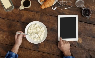 Adam ahşap masa üzerinde evde, üstten görünüm kahvaltı tablet bakıyor