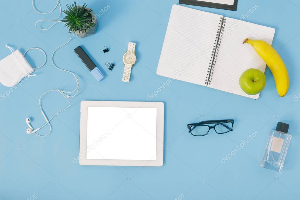 Feminine office workspace concept, white tablet and notebook with fruits and clipboard with headphones on blue table 