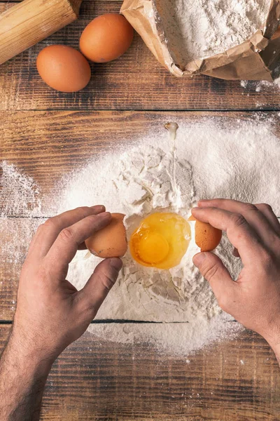 Male hands beating egg yolk into flour on wooden table, top view