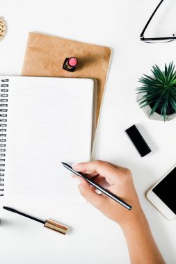 Kadın aksesuarları ile defter ve beyaz masa üzerinde kalem tutan kadın el. Kavram kadınsı çalışma yer