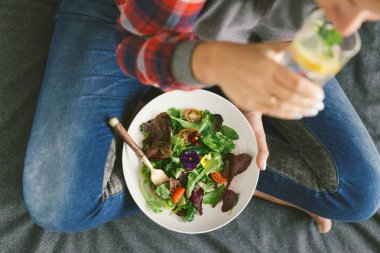 Genç kadın içme suyu limonlu sebze ve çiçekler nasturtium ve menekşe yatak, en iyi görünüm, sağlıklı gıda kavramı yaz salatası yerken