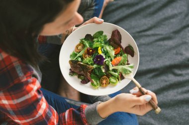 Genç kadın yaz salatası sebze ve çiçekler nasturtium ve menekşe yatak, üstten görünüm otururken yeme 