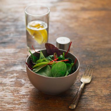 Vegetarian biodynamic food concept. Close up bowl of salad with spinach leaves and beet leaves on dark wooden table with glass of water with lemon clipart