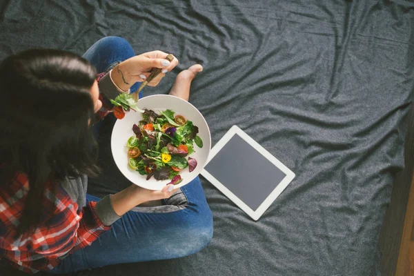 Young woman eating summer salad with vegetables and flowers nasturtium and violets sitting on bed, top view. Copy space — Stock Image Young Woman Eating Summer Salad Vegetables Flowers Nasturtium Violets Sitting Stock Picture