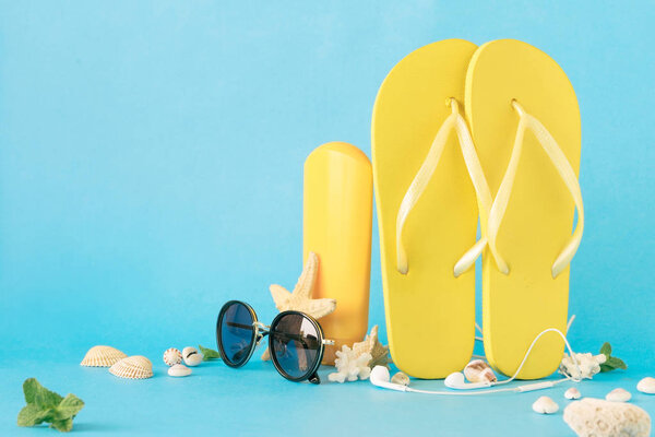 Fashion sunglasses with flip flops and beach accessories on blue background