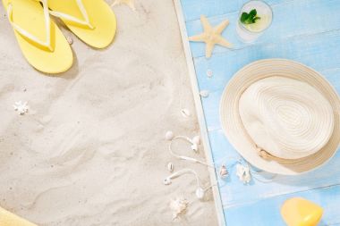 Çerçeve hasır şapka, flip flop, güneş kremi, havlu, deniz kabuklarını, yaz kokteyl. Kum üzerinde seyahat aksesuarları. Seyahat tatil kavramı. Yaz arka plan