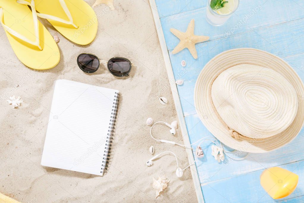 Set traveler accessories. Blank notepad with straw hat, sunglasses, flip flops, cocktail, sunblock, headphones on sand. Travel vacation concept. Summer background