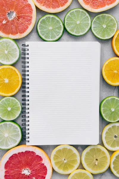 Top view of notebook with sliced citrus fruits on light background
