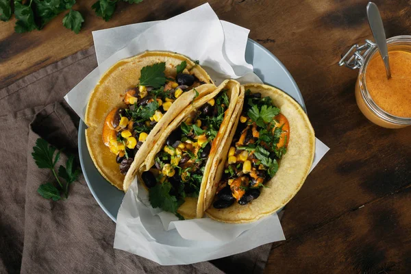 Vegetarian tacos made with corn tortillas with black beans, corn, pepper and spicy sauce served on plate, top view