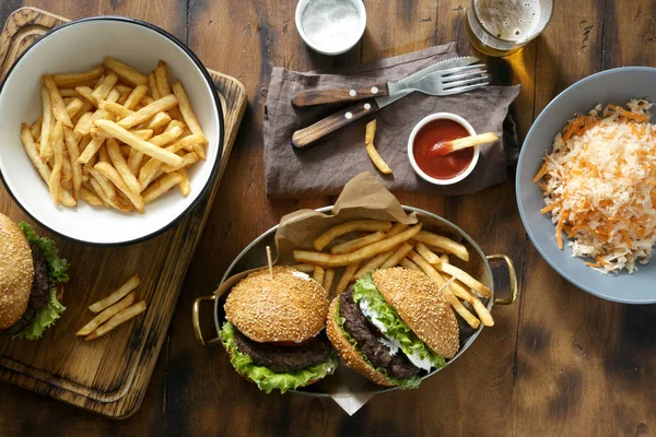 outdoor table with burger, french fries, salad and snacks on wooden table with beer