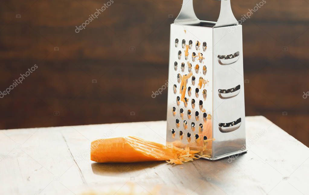 Close view of grater with carrots on wooden table