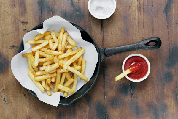 French fries served in frying pan on wooden table with ketchup, top view