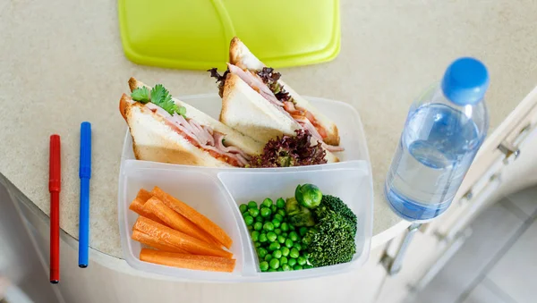 Prepared school lunch at lunch box with bottle of water in home kitchen