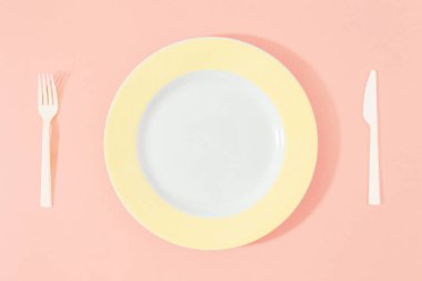 Bıçak ve çatal pembe bir arka plan üzerinde sarı plakalı. Üstten görünüm, düz yatıyordu. Diyet en az kavramı