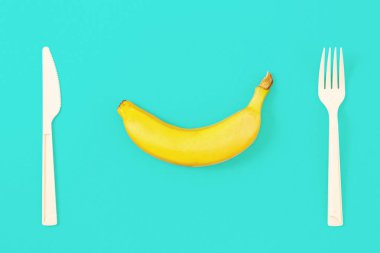 Olgun muz çatal ve bıçak ile mavi arka plan üzerinde. Üstten görünüm, düz yatıyordu