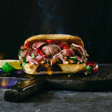 Copy alanı ile karanlık arka plan üzerinde ahşap kesme tahtalarında yangın alev ızgara baharatlı biftek sandviç