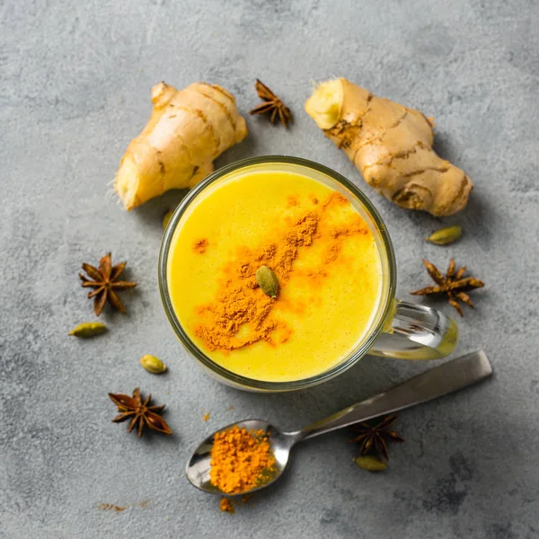 Golden yellow latte on light background. Indian drink turmeric golden milk in glass. Copy space Top view