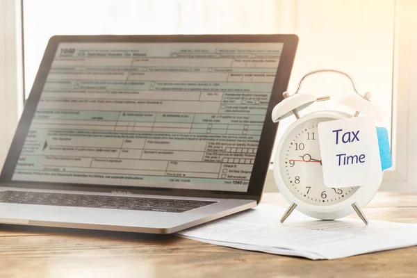 Tax Time Concept. Alarm clock with note reminder of the need to file tax returns, tax form