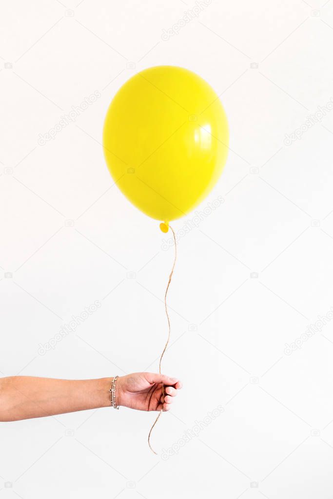 Female hand holds yellow balloon on white background. Minimal party concept
