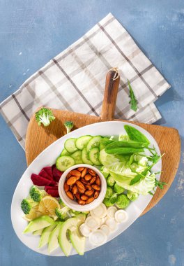 Bir tabak taze vejetaryen yemeği. Tabak manzaralı çeşitli sebzeler ve fındıklar.