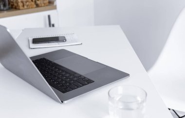 Bilgisayarı, not defteri, bir bardak suyu ve akıllı telefonu olan ev ofisi. Uzak çalışma veya çevrimiçi öğrenme kavramı 