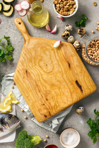 Healthy food background. Wooden board with various wholesome food. Fresh fish, vegetables, herbs and legumes on gray background top view