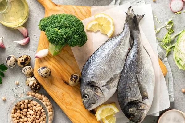 Raw cooking ingredients for tasty and healthy food. Fresh fish, vegetables, herbs and legumes on gray background top view