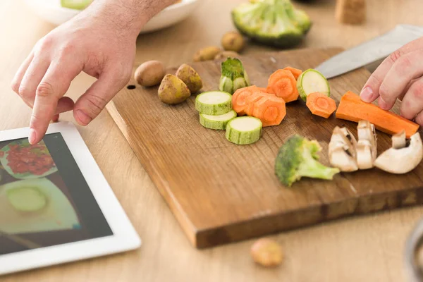 Cooking online or learning cooking concept. Man preparing vegan dish while watching recipe on the Internet using tablet