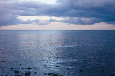 Taşlar ve gök gürültüsü bulutlarıyla deniz kıyısının panoramik görüntüsü