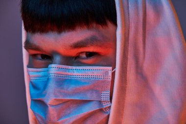 Siyah arka planda, tıbbi maskeli ve beyaz elbiseli bir adamın yakın çekimi.