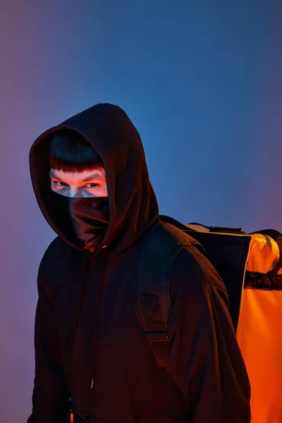 delivery man in black clothes with a yellow backpack on a colored background